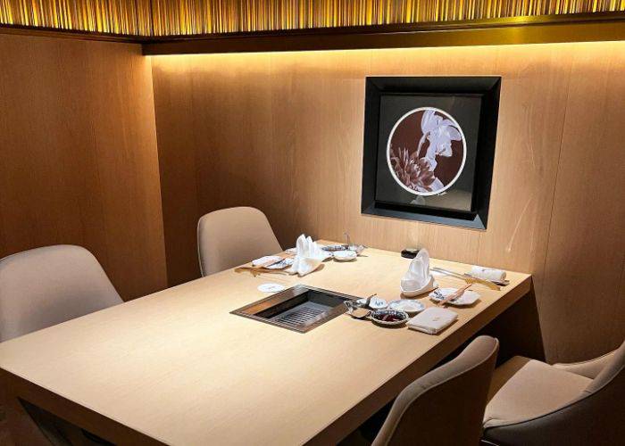 A stylish dining area at Setsugekka Tanaka Satoru, featuring an in-table grill, place settings and traditional art on the wall.